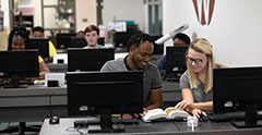 Students looking at a book in a computer lab.